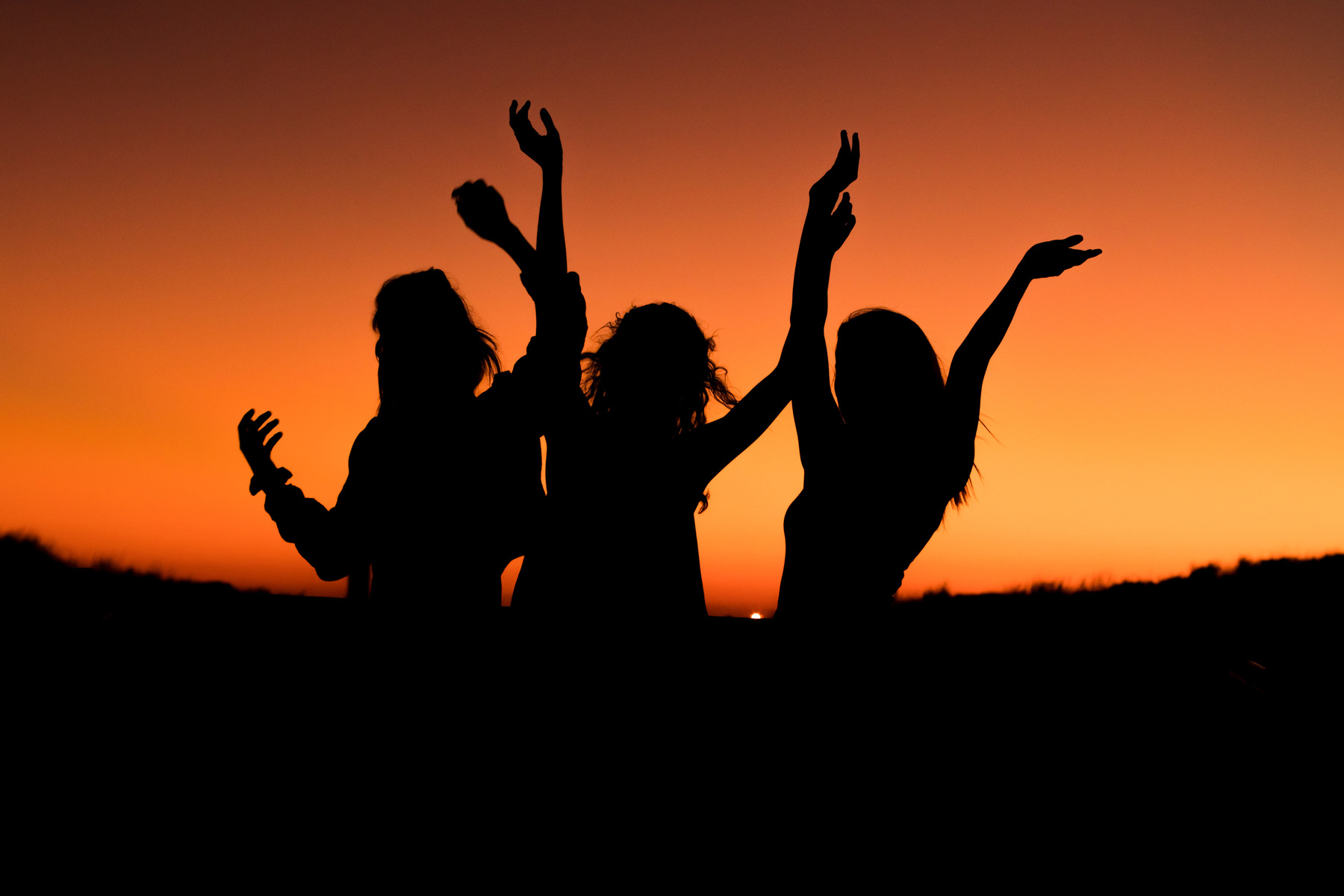 A photo of a silhouette of three people dancing as the sun sets
